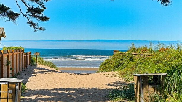 A sandy beach path leading to the ocean with wooden structures on either side. - Newly Renovated+Fire Table+Steps from Cannon Beach (Cannon Beach)