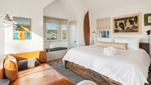 A bedroom with a large bed, a leather sofa, and artwork on the walls. - Newly Renovated+Fire Table+Steps from Cannon Beach (Cannon Beach)
