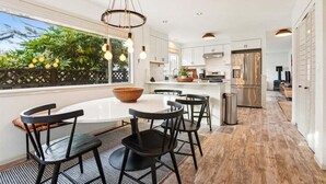 A modern kitchen with white cabinets, a stainless steel refrigerator, and a dining area with a round table and black chairs. - Newly Renovated+Fire Table+Steps from Cannon Beach (Cannon Beach)