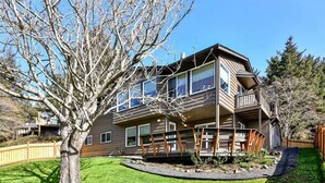 A two-story house with a deck, a large tree in the yard, and a clear blue sky.