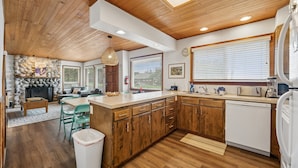 A modern kitchen with wooden cabinets, a central island, and a stone fireplace. - Shutterbug - 1 Block to the Beach! (Arch Cape)
