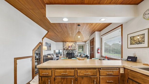 A kitchen with wooden cabinets, a central island, a stone fireplace, and a dining area in the background. - Shutterbug - 1 Block to the Beach! (Arch Cape)