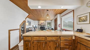A kitchen with wooden cabinets, a central island, a stone fireplace, and a dining area in the background.