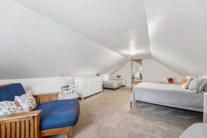 Ein Schlafzimmer mit schrägem Dach, einem Bett, einem Sessel, einer Kommode und einem kleinen Tisch.