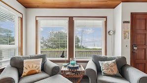 A room with two grey sofas, a wooden coffee table, and a view through large windows. - Shutterbug - 1 Block to the Beach! (Arch Cape)