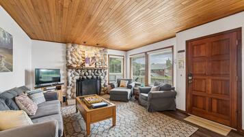 A living room with a stone fireplace, wooden ceiling, grey sofas, a coffee table, and a television.