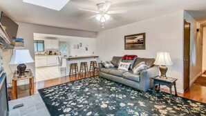 A living room with a sofa, a coffee table, a TV, and a ceiling fan. There is a kitchen in the background with a bar counter. - D & D Retreat - Quiet Neighborhood! (Cannon Beach)