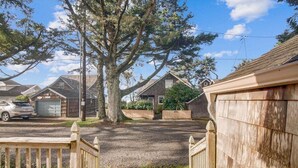 A residential driveway with a wooden gate, a large tree, and houses in the background. - The Walter House - Quiet Neighborhood! (Cannon Beach)