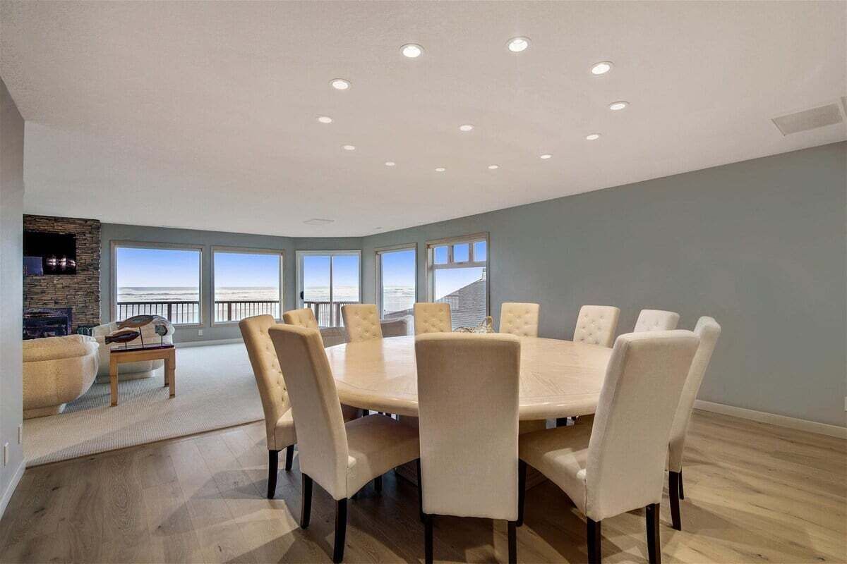 Un vaste espace dédié à la salle à manger, avec une table ronde et de nombreuses chaises, de grandes fenêtres offrant une vue dégagée et une cheminée en pierre.
