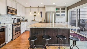 Una cocina moderna con electrodomésticos de acero inoxidable, una isla de mármol con taburetes y un amplio ventanal que proporciona luz natural.