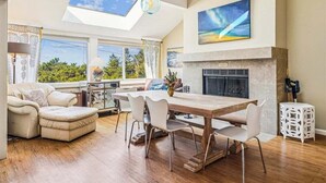 Un salón comedor amplio con techo alto, chimenea, zona de comedor y ventanas grandes que ofrecen vistas al exterior.