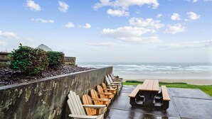 A beachside patio with wooden chairs and a picnic table, overlooking the ocean.