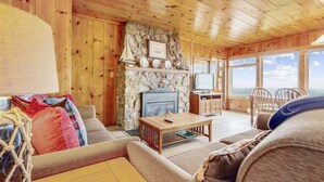 A cozy cabin interior with a stone fireplace, wooden walls, and a view of the ocean.