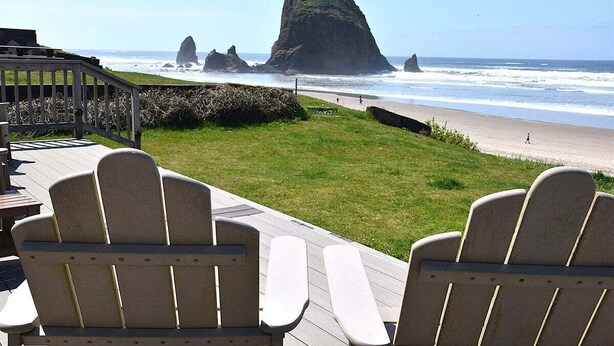 Una terraza con sillas Adirondack que da a una playa con una formación rocosa destacada.