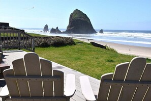 Une terrasse dotée de chaises Adirondack, donnant sur une plage et offrant une vue sur une formation rocheuse remarquable.