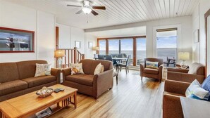 Amplia sala de estar con piso de madera, sofás marrones, una mesa de centro y un comedor con vistas al océano.