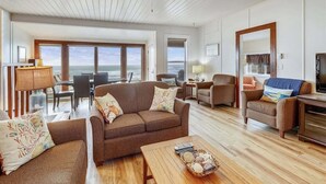Amplia sala de estar con un ventanal que da al mar, amueblada con un sofá, sillas y una mesa de centro.