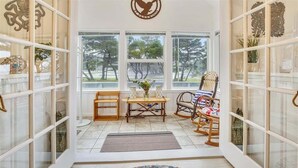 A room with a large window, a wooden table with chairs, a rocking chair, and a colorful rug. - Sandy Owl - Close Beach Access! (Cannon Beach)