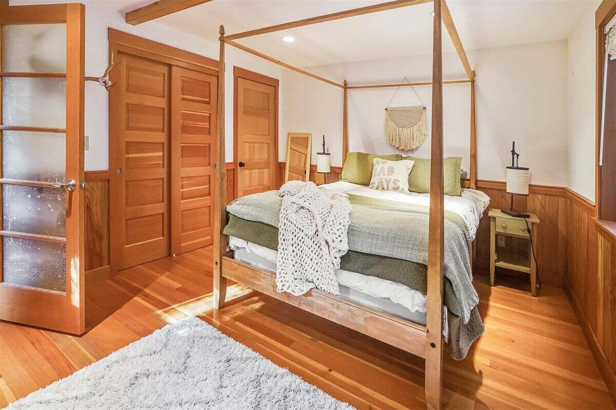 Uma cama de dossel com cortina, piso de madeira e um tapete branco felpudo.