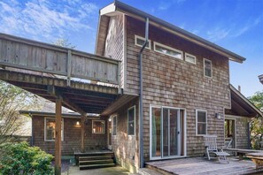 A two-story wooden house with a covered porch, large sliding glass doors, and a small deck area. - Salal Bungalow - Close to Beach & Downtown! (Cannon Beach)