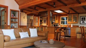 Ett mysigt vardagsrum med en brun lädersoffa, ett runt soffbord och en köksdel med träskåp och ett kylskåp.