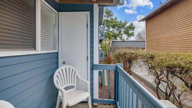 A covered porch with a white chair, a door, and a blue railing. - Sandcastle Inn #601 - Downtown Apartment! (Cannon Beach)