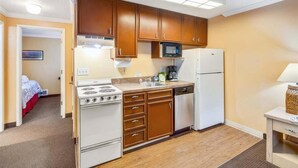 Una cucina compatta con mobili in legno, un piano cottura bianco, un forno a microonde ed una lavastoviglie.