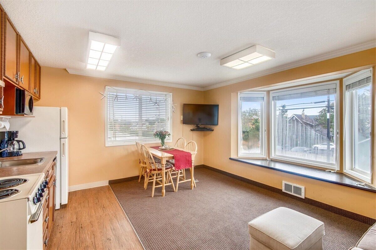 A compact kitchen with a dining area, a TV, and large windows.