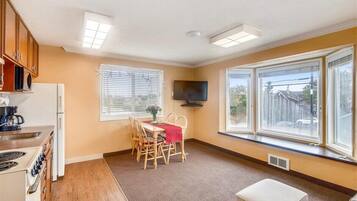A compact kitchen with a dining area, a TV, and large windows.