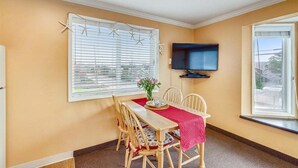 Un espace repas comprenant une table, des chaises, un téléviseur et une fenêtre avec des stores.
