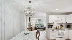 Eine moderne Küche mit weißen Schränken, einem Essbereich mit Tisch und Stühlen sowie einer Pendelleuchte.