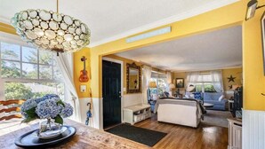 Un salón amplio con suelo de madera, una mesa de comedor con un jarrón de flores, una guitarra y un espejo en la pared.