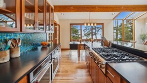 A modern kitchen with wooden cabinets, a large island, and a view of the outdoors. - Santo Cristo - Ocean View! (Arch Cape)