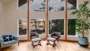 A spacious room with large windows, two armchairs, a small table, and a potted plant. - Santo Cristo - Ocean View! (Arch Cape)
