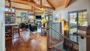 Un vaste espace de vie doté d’un plafond en bois, un coin repas avec une table et des chaises, et un escalier muni d’une rampe.