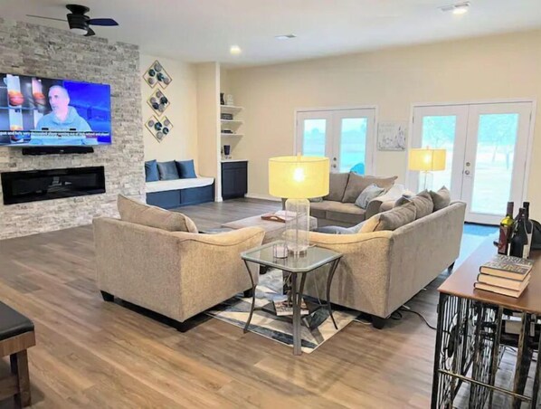 A modern living room with two sofas, a coffee table, a TV mounted on a stone wall, and a dining area with a table and chairs.