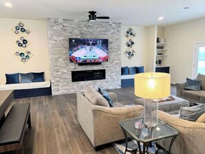A modern living room with a stone accent wall, a flat-screen TV mounted above a fireplace, and a glass coffee table.
