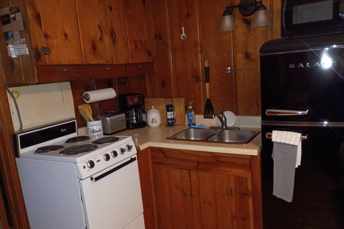 A compact kitchen with wooden cabinets, a white stove, a sink, and a black refrigerator.
