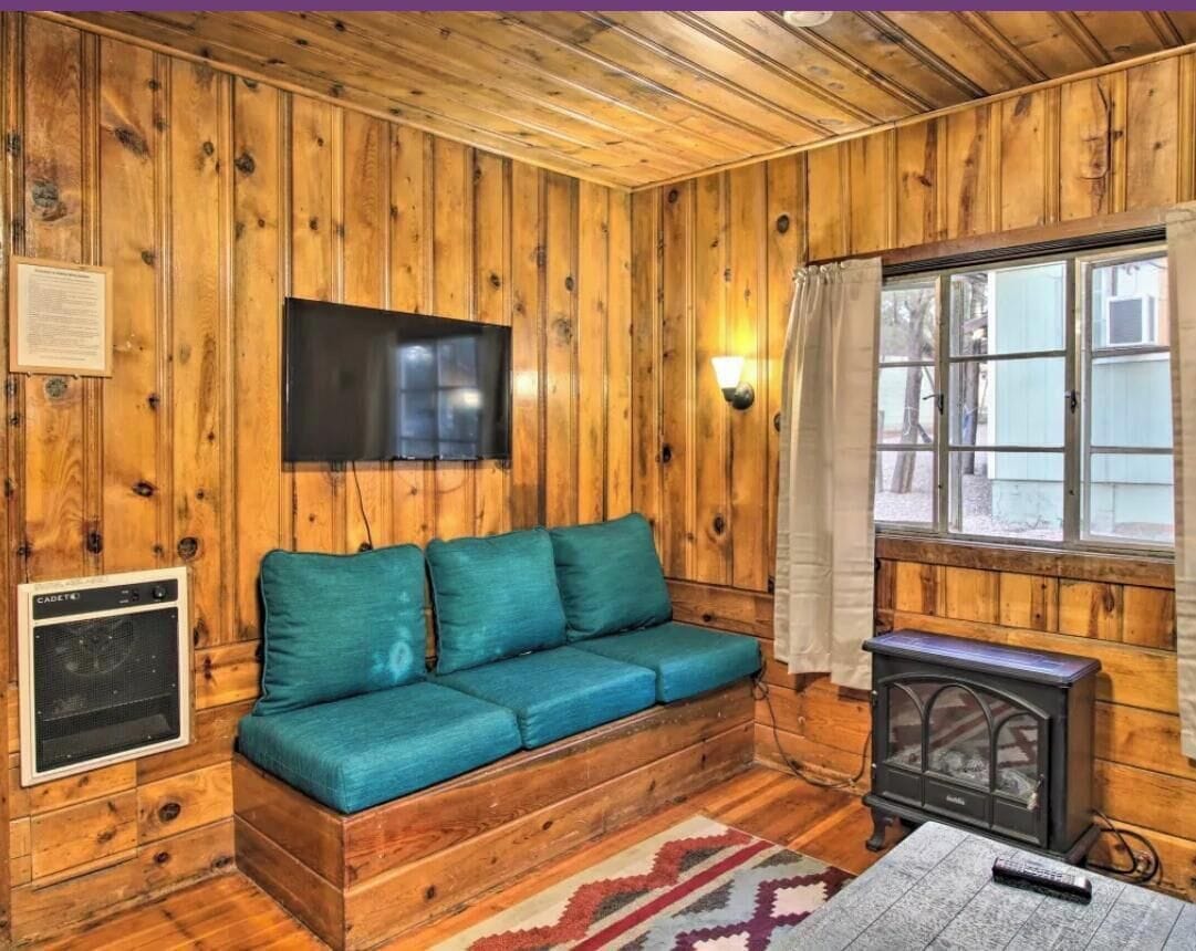 A wooden cabin interior with a sofa, a television, a heater, and a window.