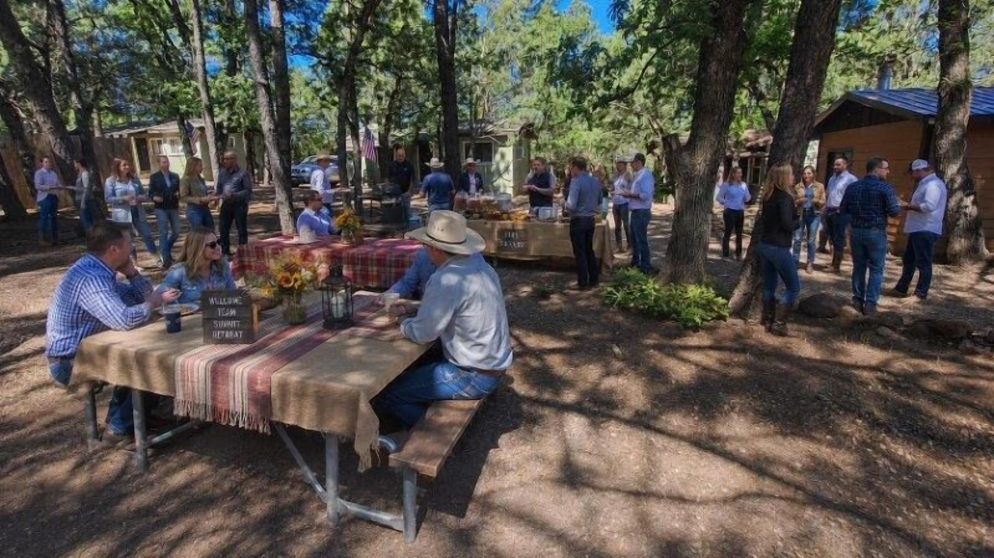 Un área de comedor al aire libre con mesas, bancos y un cartel de bienvenida.