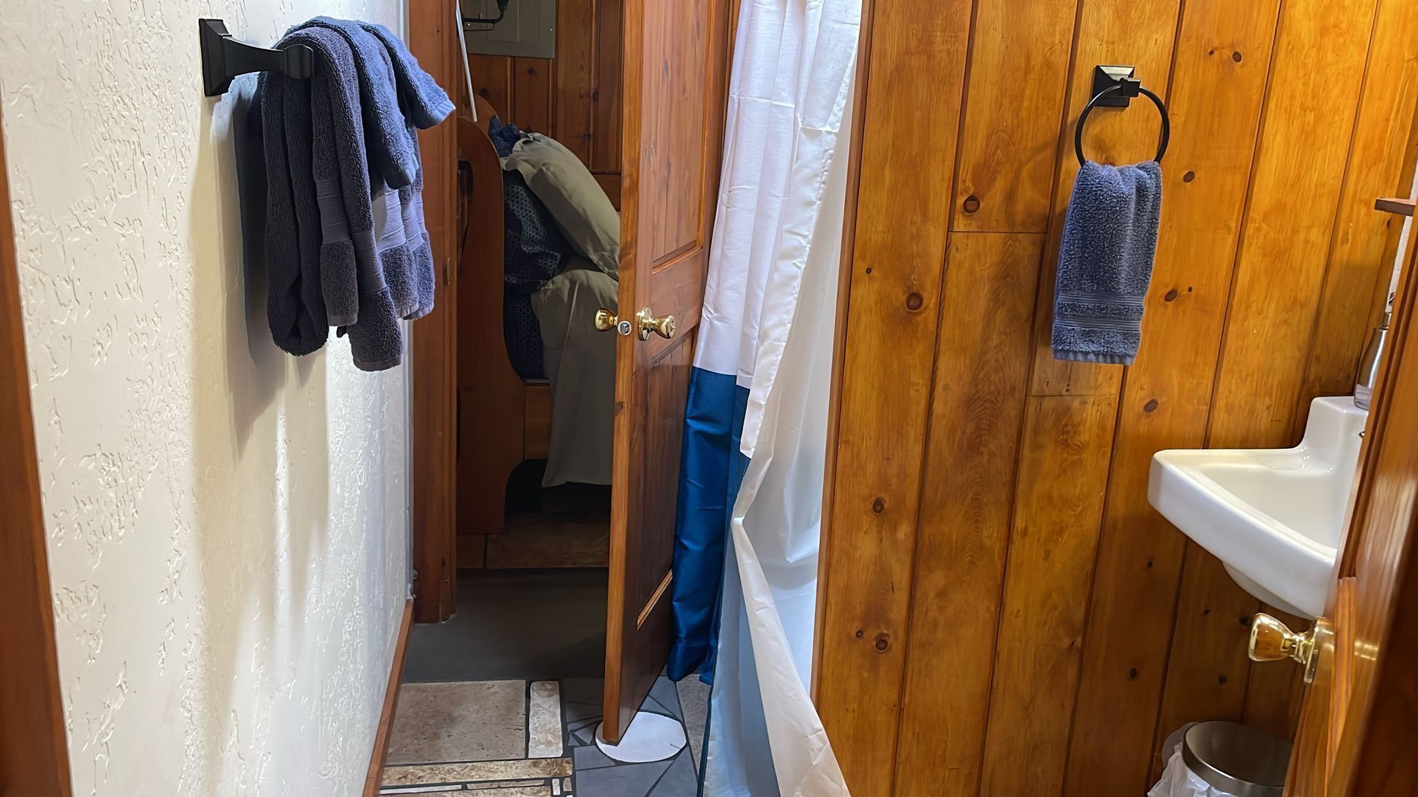 A narrow bathroom with wooden walls, a white sink, and a shower curtain.