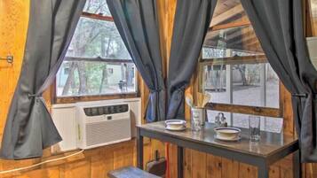 Interior de madeira com uma janela, uma mesa com pratos e um banco.