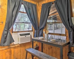 Interior de madera con ventana, una mesa con platos y un banco.
