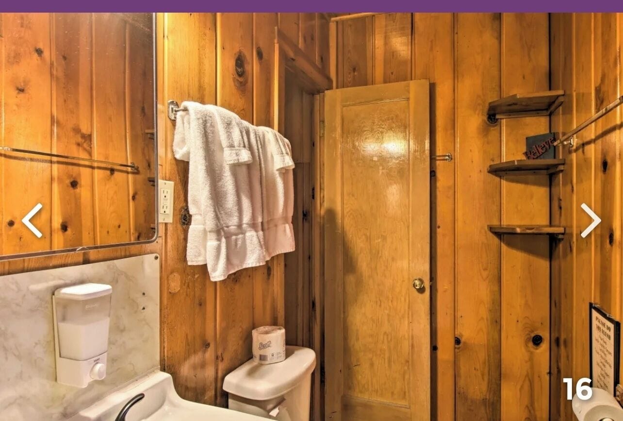 A wooden-paneled bathroom with a toilet, a towel rack, a soap dispenser, and a toilet paper holder.