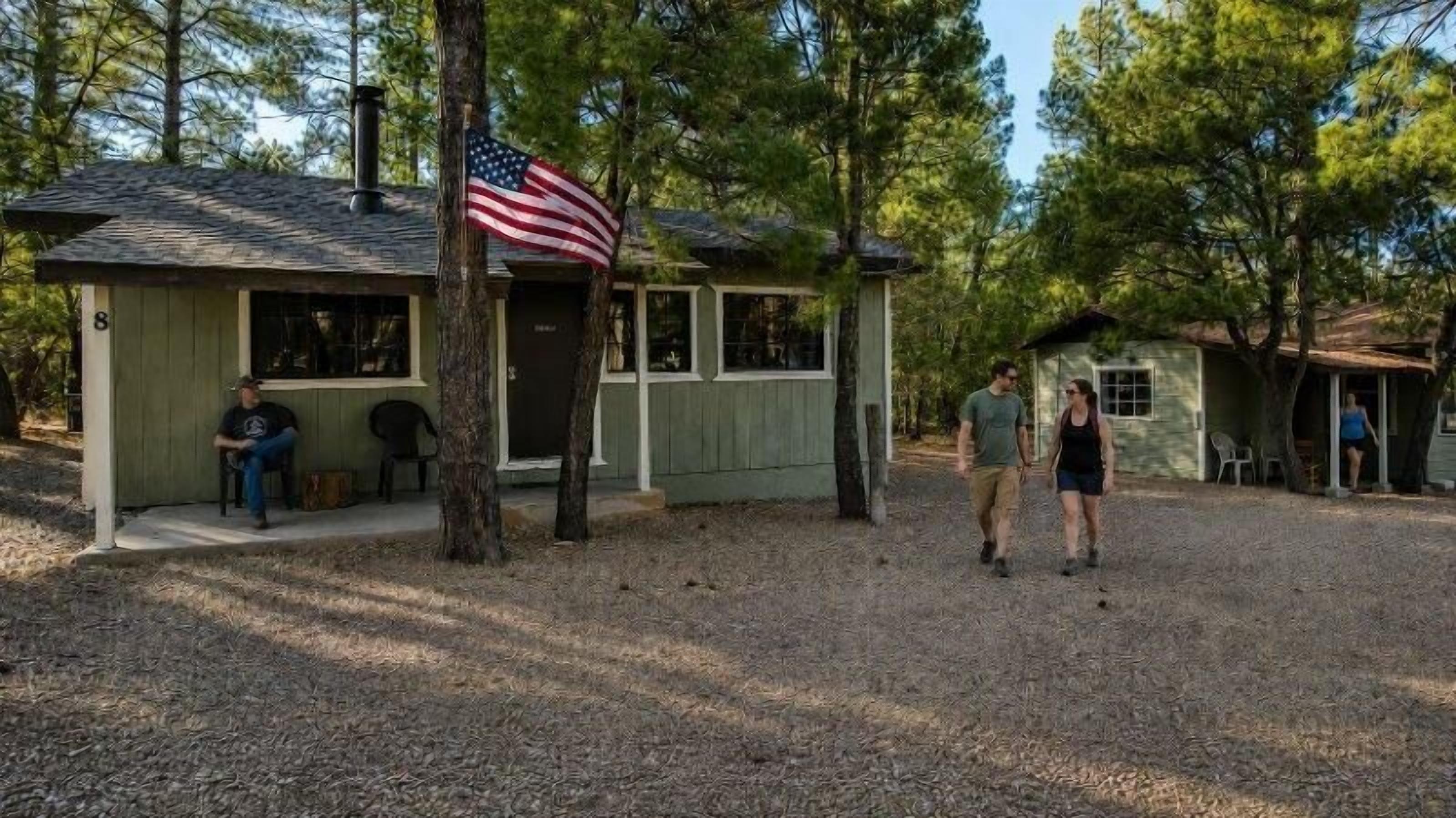 Une cabane avec une véranda, un drapeau américain et une personne assise à l’extérieur.