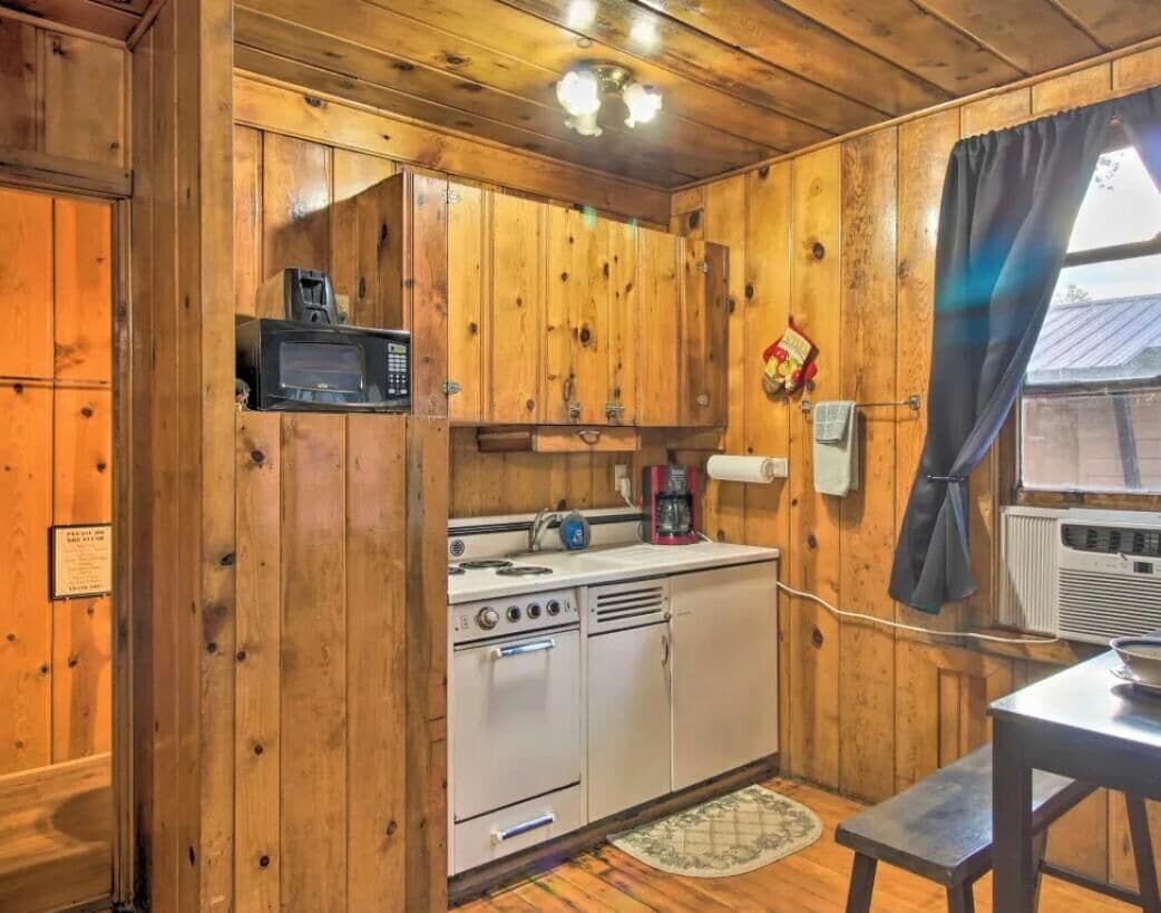 A wooden cabin interior with a kitchenette, including a microwave, stove, and sink.
