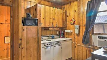 A wooden cabin interior with a kitchenette, including a microwave, stove, and sink.
