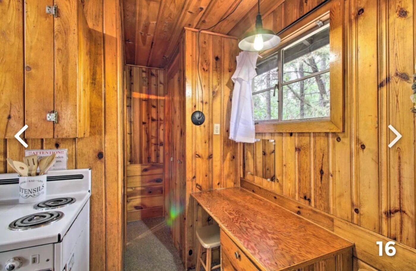 Interior de una cabaña de madera con área de cocina, una mesa de comedor y una ventana con vista a árboles.