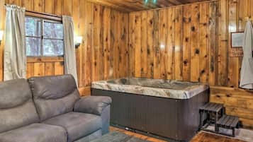 A wooden cabin interior with a sofa, a hot tub, and a ceiling fan.