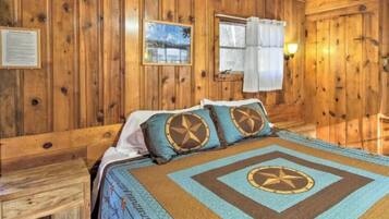 A wooden-paneled room with a bed, a nightstand, a window with curtains, and a wall-mounted light.